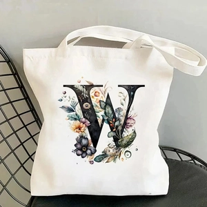 Floral letter W print on a white canvas tote bag placed on a black mesh chair