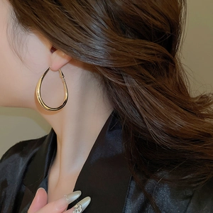 Close-up of model wearing large polished gold teardrop hoop earrings with high mirror finish