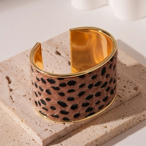 Detail of wide leopard print bangle with polished gold inner band on stone surface