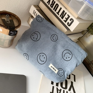 Blue corduroy storage bag with black smiley faces shown in a minimalist home setup