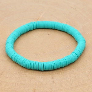 Detailopname van een turquoise heishi-kralenarmband op een lichte houten basis