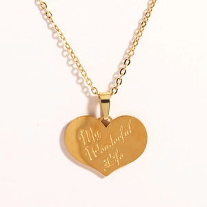 Detail of a gold heart pendant necklace engraved with My Wonderful Life on white background