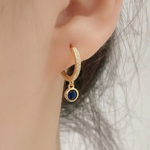 Close-up of gold hoop earring with blue round gemstone and zircon accents on model