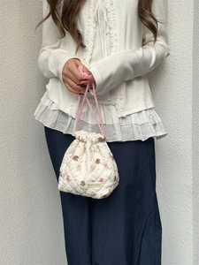 Close-up of a white quilted drawstring bag with bear and floral pattern held by a model