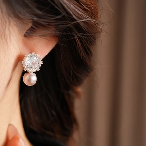 Close-up of pearl earrings with zircon flower studs worn on a model earlobe