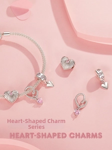 Macro shot of silver heart charms and a pink zircon pendant on a woven snake chain bracelet