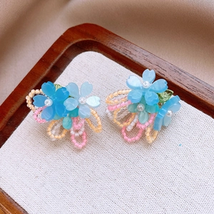 Détail de boucles d'oreilles fleurs en résine bleue et perles sur un plateau en bois