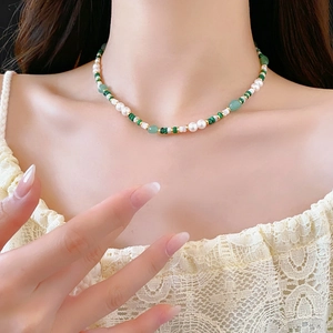 Close-up of pearl and malachite green bead necklace worn by a model on lace