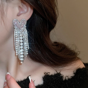 Close-up of sparkling heart tassel earrings with silver finish on female model