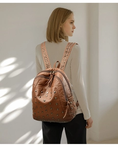 Detail view of brown leather backpack with metal rivets on a model in soft light