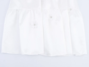 Close-up of white satin hem featuring ruffled edges with 3D floral accents and rhinestones
