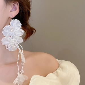 Detail of oversized white petal earrings with pearls and long flowing tassel chains