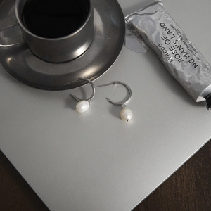 Elegant silver pearl earrings displayed on a metallic surface with lifestyle accessories