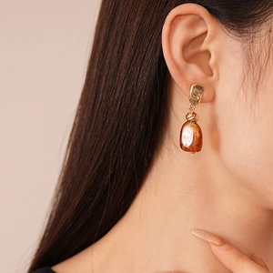 Close-up of model wearing gold irregular texture earrings with amber resin pendants