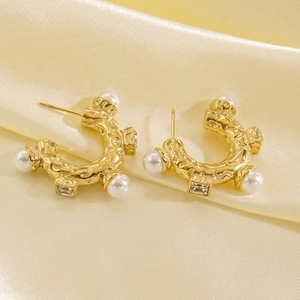 Detail of C-shaped gold-tone earrings with pearls and crystals on yellow satin fabric