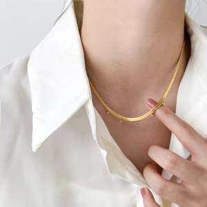 Close-up of golden snake chain necklace with small metal beads on a white shirt