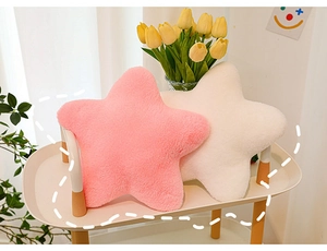Plush star pillows in pink and white on a wooden side table with fresh tulips