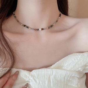 Detail of beaded necklace with gray wood beads and a central white pearl on a model