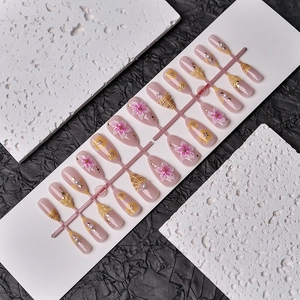 Close-up of pink almond press-on nails with 3D cherry blossoms, pearls and gold foil