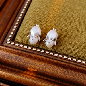Detailed shot of silver flower bud earrings with white pearls on a green fabric backdrop