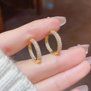 Detailed close-up of gold hoop earrings with pavé set cubic zirconia held in hand