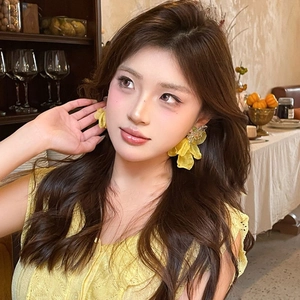 Macro detail of a yellow chiffon flower earring on a model in a knit sweater