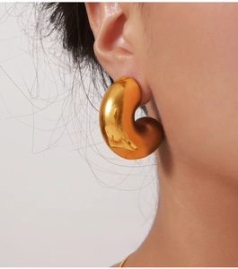 Macro close-up of chunky gold-plated C-shaped earrings with a polished mirror finish