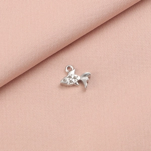 Close-up of a silver fish charm with shimmering crystals on pink fabric texture