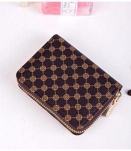 Detail showing deep brown mini card wallet with golden clover patterns and metal zipper