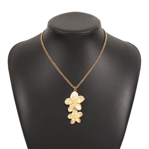 Detail of golden necklace featuring double floral pendants on a black neck display stand