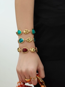 Macro shot of gold plated water drop resin bracelets and rings on model's hand