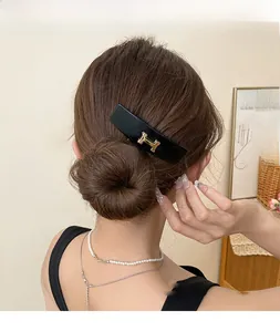 Detail of vintage black acrylic hair clip with gold H logo on dark brown hair bun