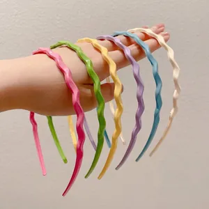 Set of six colorful wavy thin headbands in candy colors held against a plain wall