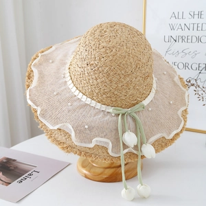 Dettaglio di cappello in paglia a tesa larga con pizzo, perle e ciondoli a tulipano