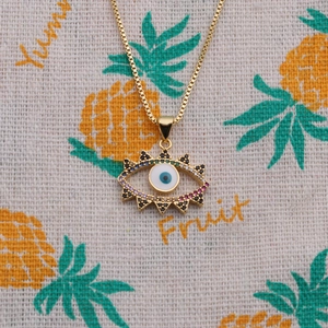 Detail of gold box chain necklace with evil eye pendant and colorful zircons