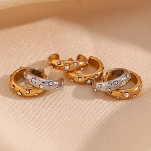 Detail of C-shaped gold and silver earrings with inlaid rhinestones on fabric