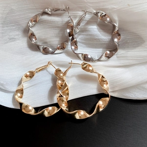 Détail de boucles d'oreilles créoles torsadées dorées et argentées sur tissu texturé