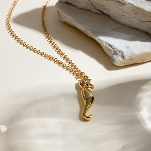 Detailed view of a gold seahorse pendant necklace with a small gemstone eye on a natural stone