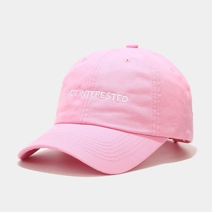 Close-up of white 'NOT INTERESTED' embroidery on pink cotton twill baseball cap