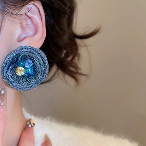 Close-up of a blue woven flower earring with sparkling crystals on a female model