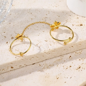 Golden double ring set with flower design connected by chain on textured stone