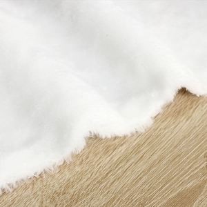 Plush white faux fur Christmas tree skirt on light wood floor for festive holiday decor