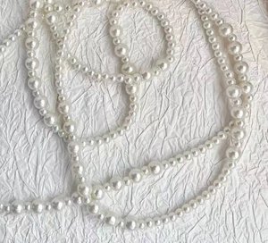 Detailed view of the lustrous white faux pearl strand necklace on white textured paper