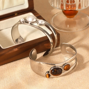 Detail of hollow stainless steel open cuff bangles with tiger eye stone and pearl accents