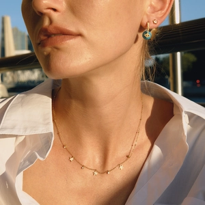 Lifestyle shot of gold star necklace and blue evil eye earring worn by model in soft light
