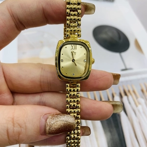 Detail shot of a small gold square watch dial with Roman numerals and diamond accents