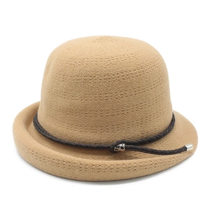 Detail of beige knit cloche hat showing woven texture and decorative leather cord with buckle