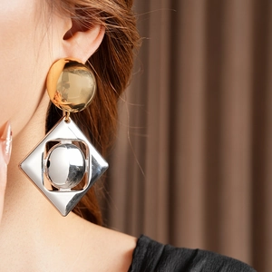 Close-up of geometric earrings featuring a gold circular stud and silver diamond drop