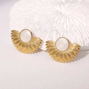 Detail shot of fan-shaped gold earrings with pearl inlay on a white textured background