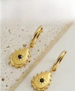 Detail of gold teardrop earrings featuring a black gemstone with starburst pattern inlay